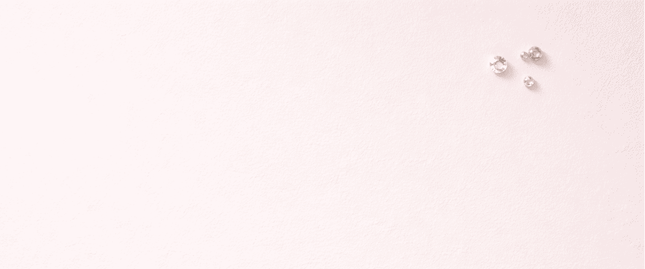 Minimal flat lay of a soft pink surface with three tiny gemstones placed in one corner and large empty space, clean luxury jewelry photography.